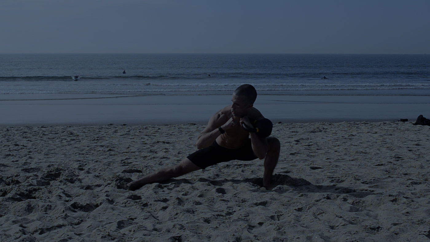 Man performing a lateral lunge with a kettlebell on the beach